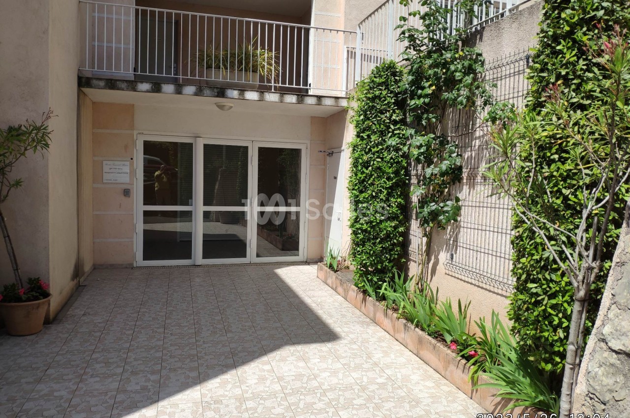 Entrée d'un immeuble résidentiel avec porte vitrée, sol carrelé et murs bordés de plantes vertes.