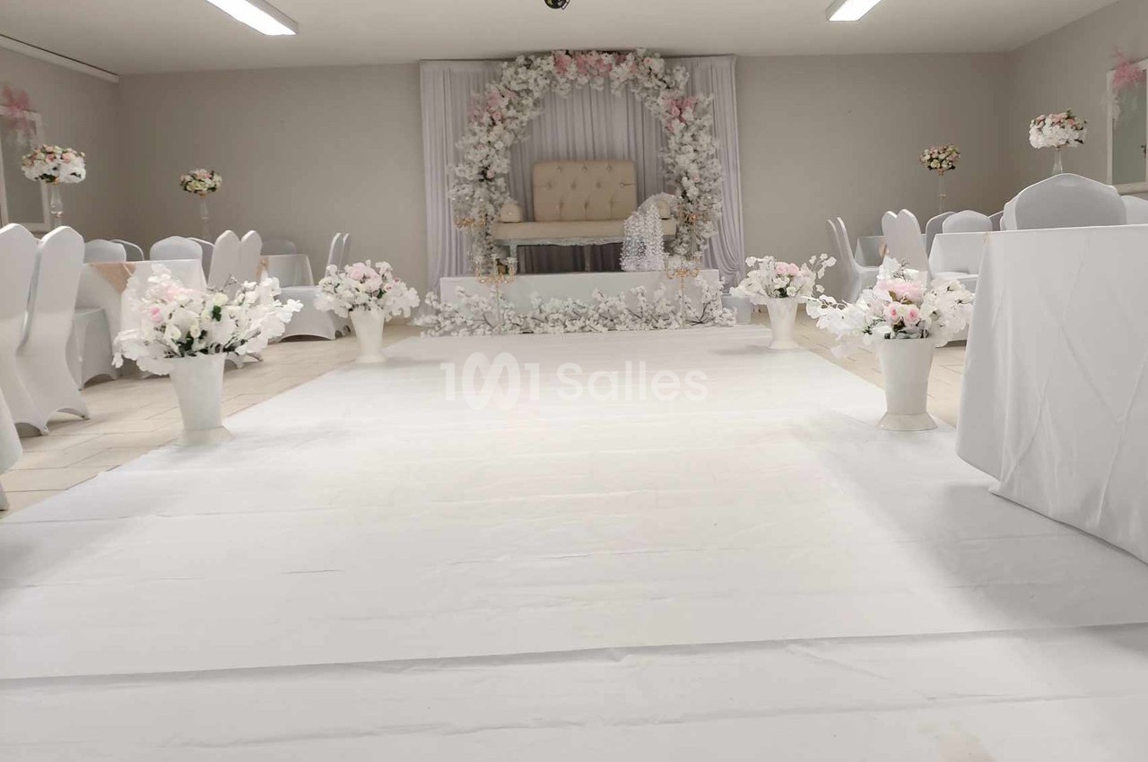 Salle de réception décorée en blanc avec des fleurs et une arche florale autour d'un fauteuil central.