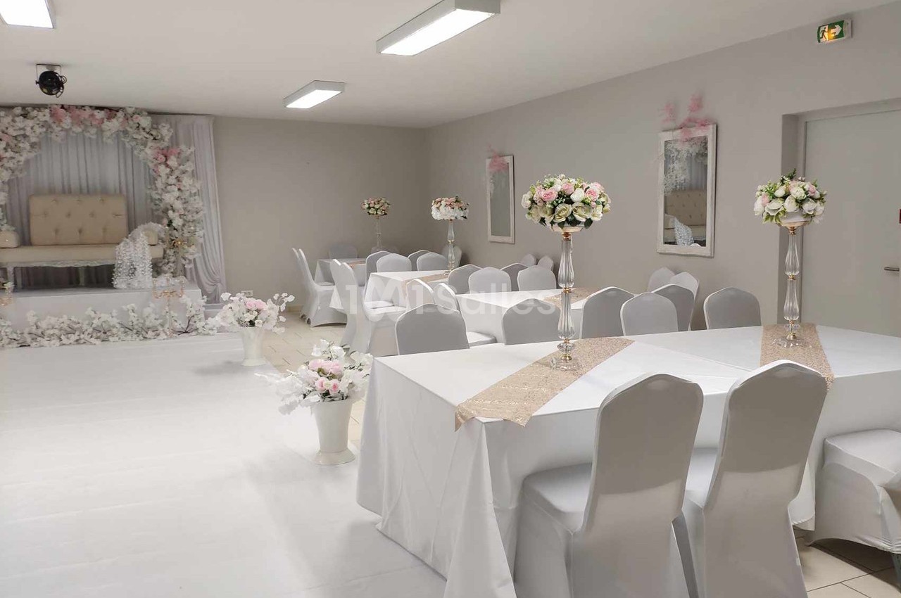 Salle de réception décorée avec des tables blanches, des chemins de table beiges et des compositions florales élégantes.