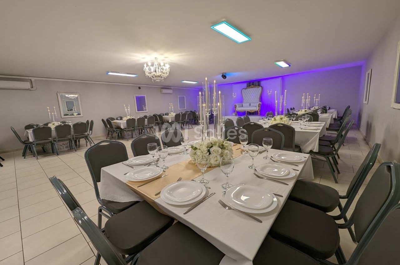 Salle de réception décorée avec des tables dressées, des chandeliers et un éclairage tamisé.