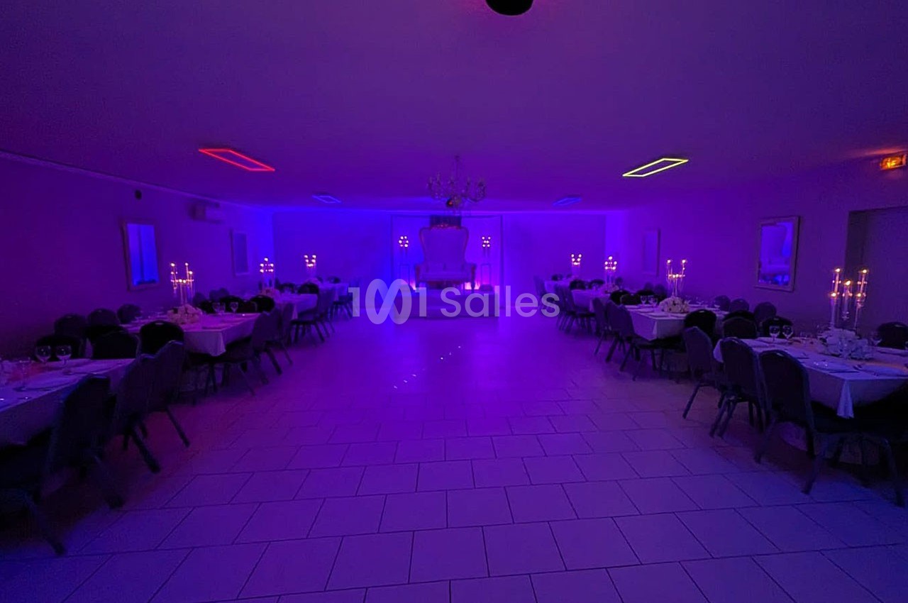Salle de réception éclairée par des lumières colorées violettes, avec tables dressées et chandeliers allumés.