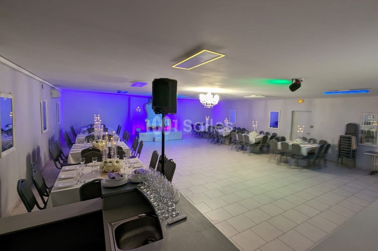 Salle de réception lumineuse avec tables dressées, chaises alignées, décorations élégantes et éclairage coloré.
