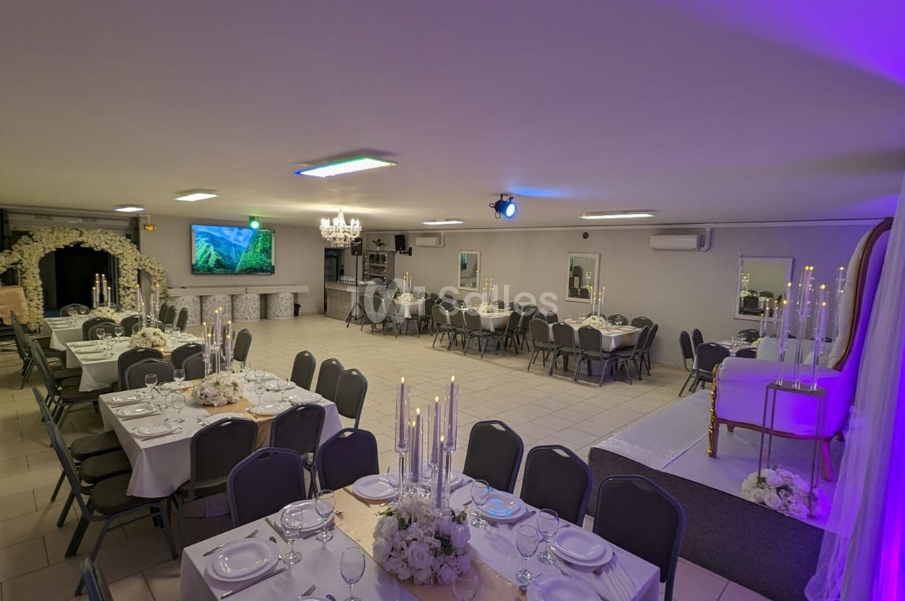 Salle de réception décorée avec des tables dressées, des chandeliers et un espace aménagé pour des événements.