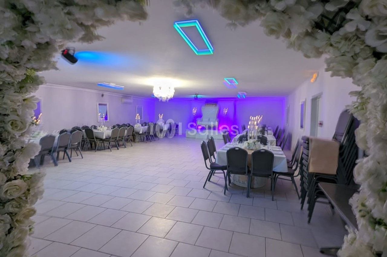 Salle de réception décorée avec des tables dressées, éclairage violet et cadre floral en premier plan.