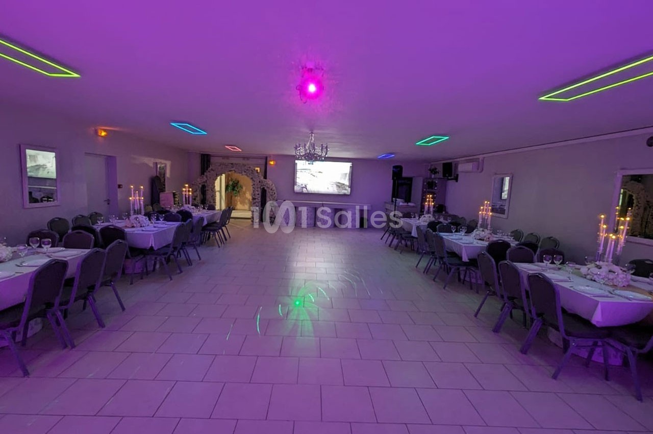 Salle de réception décorée avec des tables dressées, éclairage coloré et grand écran au fond.
