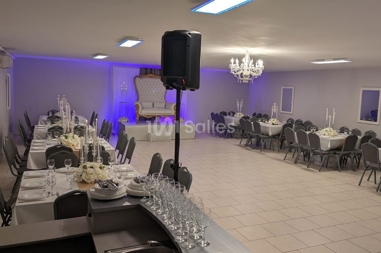 Salle de réception décorée avec des tables dressées, un trône sur une estrade et un éclairage violet.