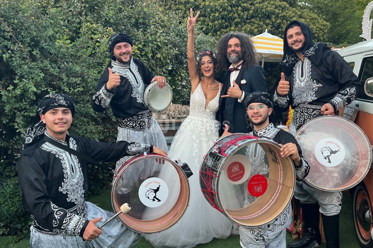 Un couple en tenue de mariage pose joyeusement avec un groupe de musiciens en costumes traditionnels.
