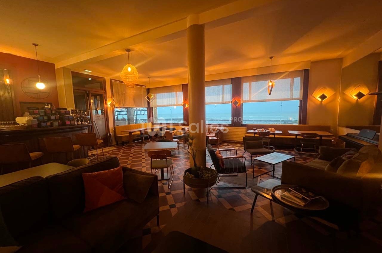 Salle de café chaleureuse avec éclairage tamisé, mobilier confortable et vue sur la mer à travers de grandes fenêtres.