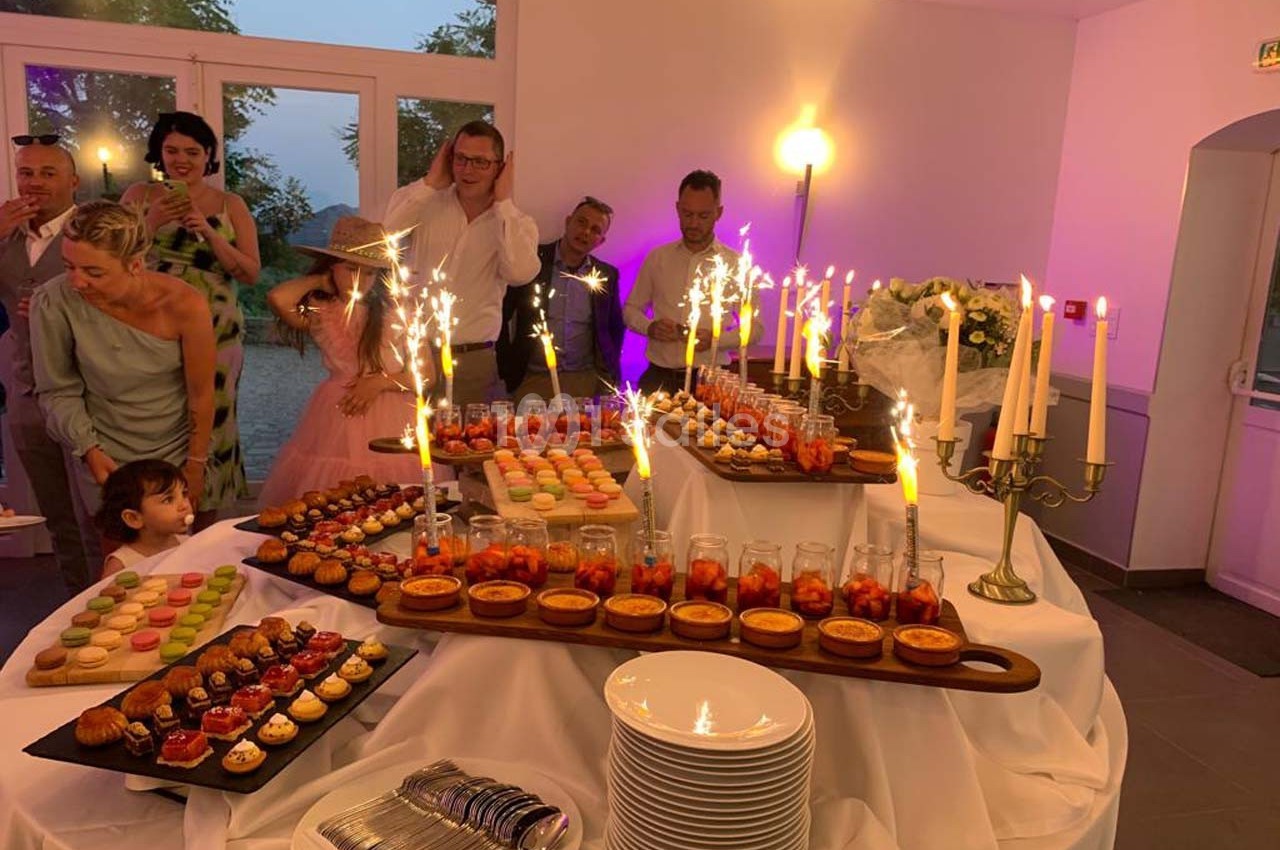 Table garnie de desserts variés avec des étincelles, entourée de convives dans une salle éclairée.