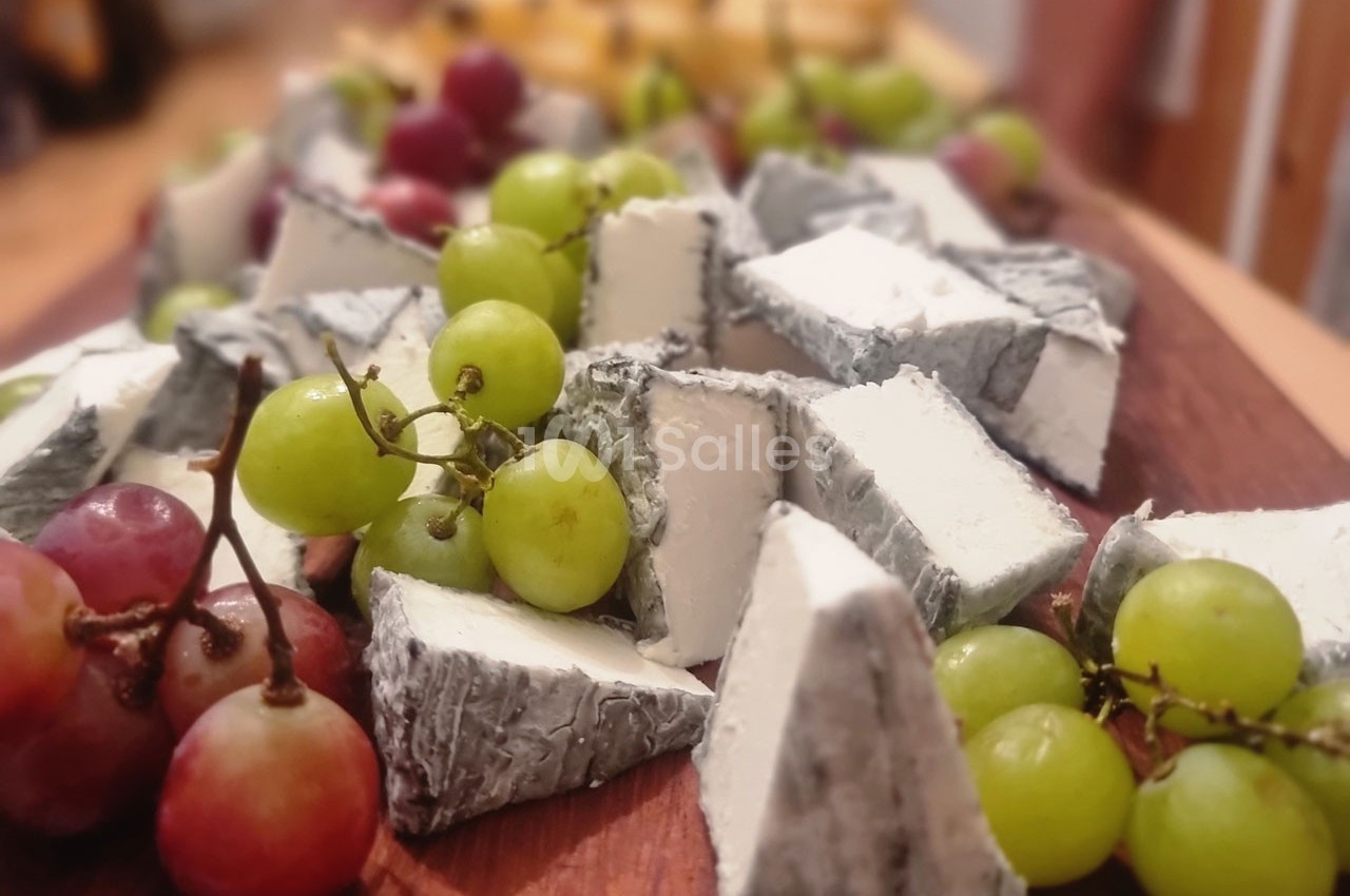 Assortiment de fromages à pâte molle avec croûte cendrée, accompagné de raisins verts et rouges sur une planche en bois.
