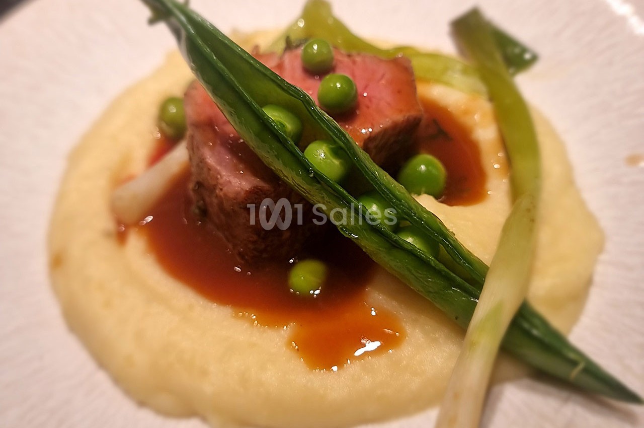 Plat composé de viande rosée, purée onctueuse, sauce brune, petits pois et oignons verts en garniture.