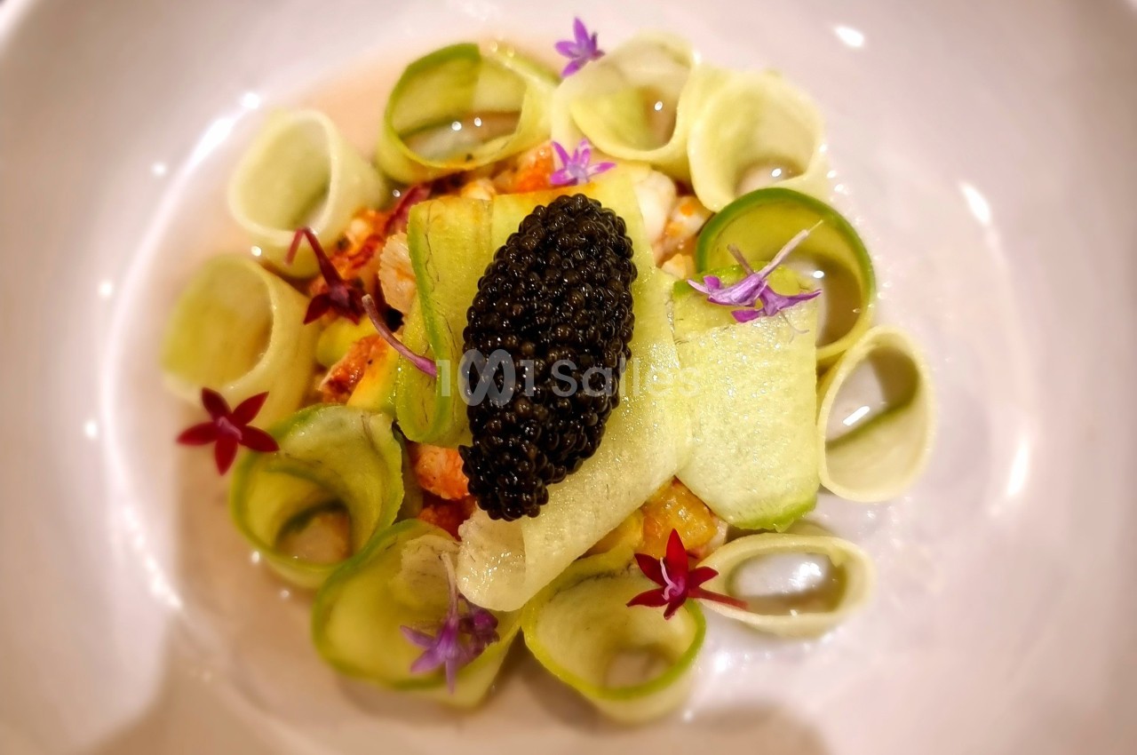 Assiette gastronomique avec caviar, rubans de légumes verts, fleurs comestibles et présentation soignée.