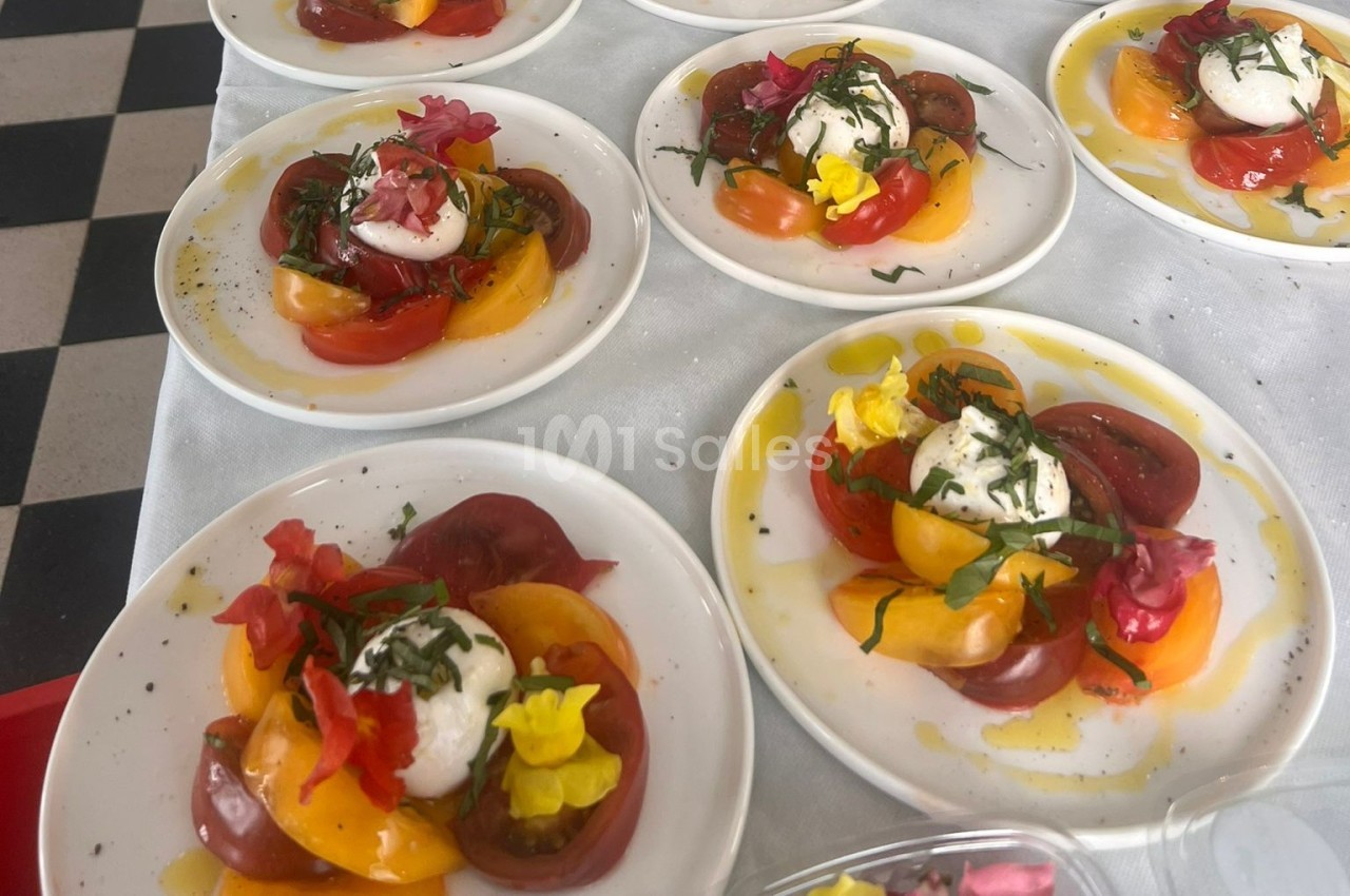 Assiettes de salade colorée avec tomates, burrata, herbes fraîches et fleurs comestibles sur une nappe blanche.