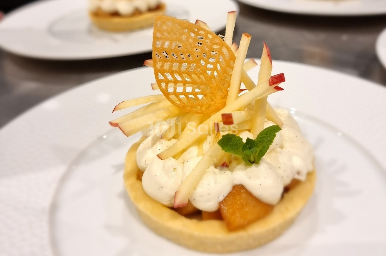Tartelette garnie de crème, morceaux de pomme, décor en dentelle croustillante et feuille de menthe.