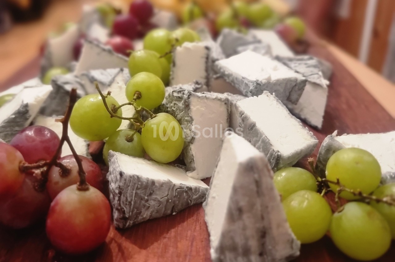 Assortiment de morceaux de fromage à croûte cendrée entourés de raisins verts et rouges sur une planche en bois.