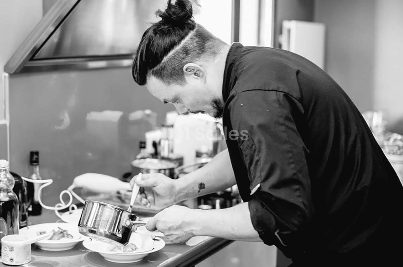 Un chef verse une sauce dans une assiette avec concentration dans une cuisine professionnelle.