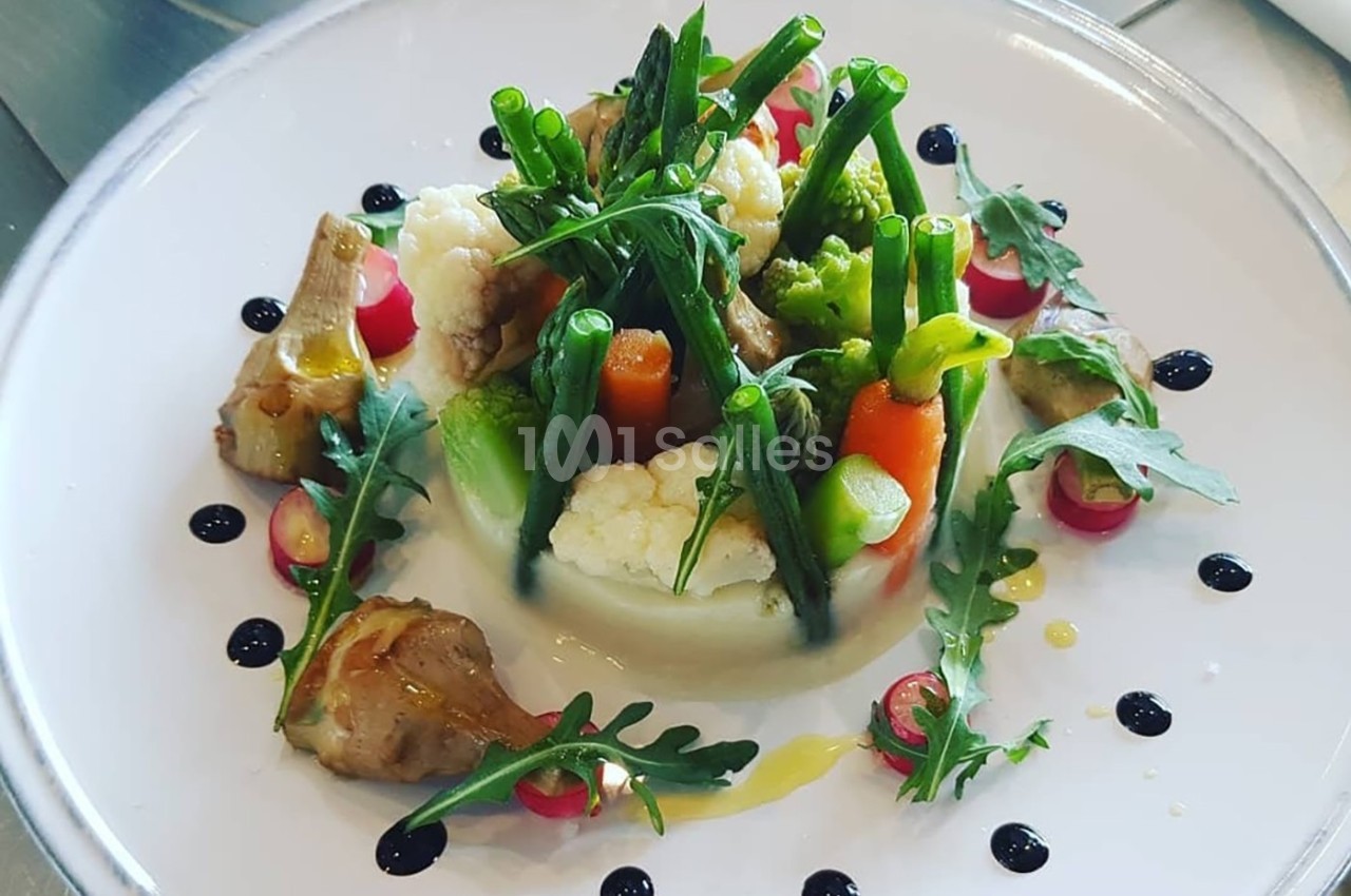 Assiette de légumes variés dressés avec soin, comprenant asperges, carottes, chou-fleur, roquette et sauce décorative.