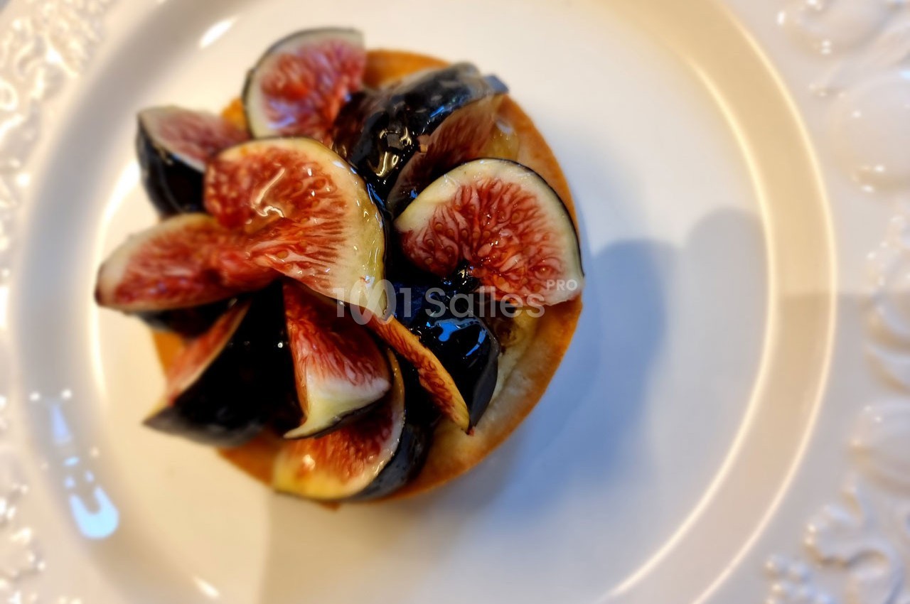 Tartelette garnie de quartiers de figues fraîches sur une assiette blanche ornée de motifs en relief.
