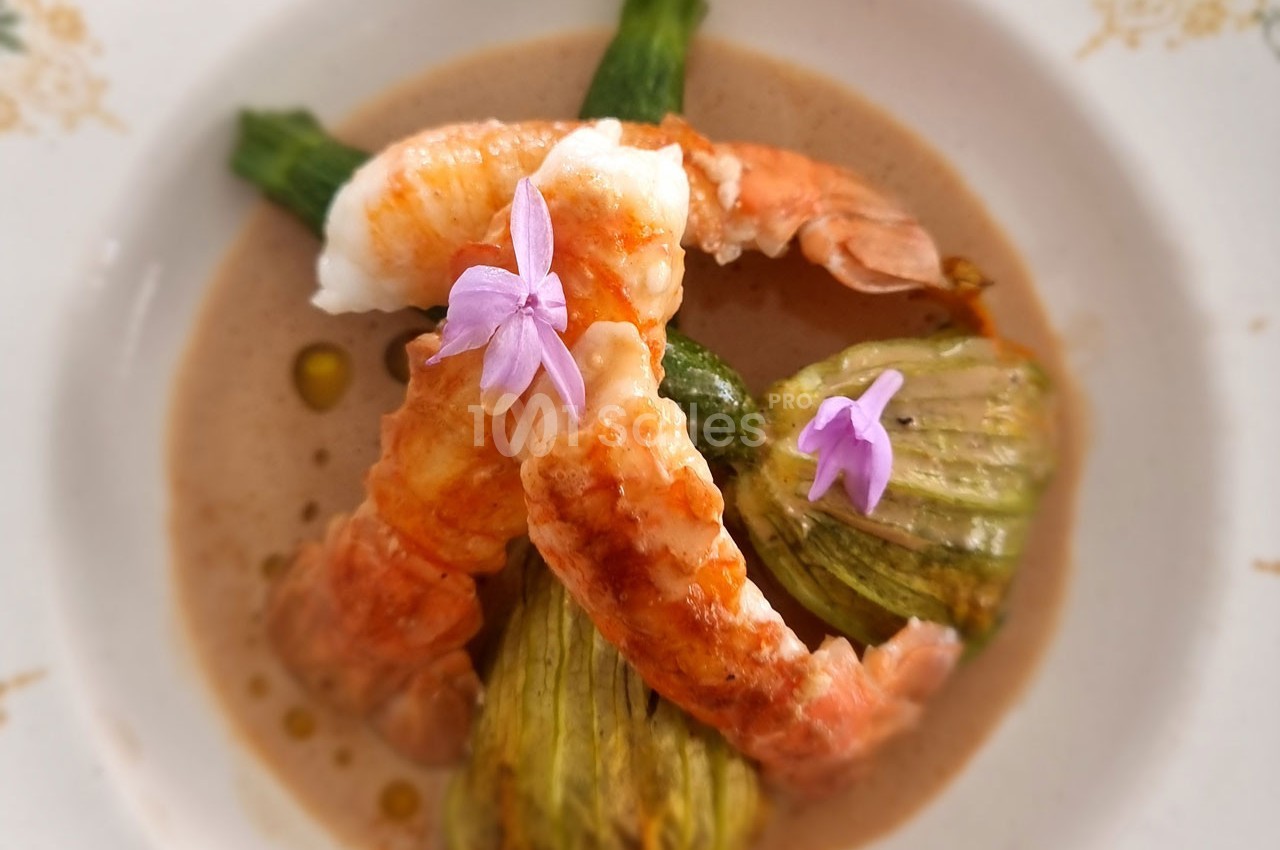 Crevettes servies avec des fleurs de courgette farcies, décorées de fleurs comestibles sur une sauce crémeuse.