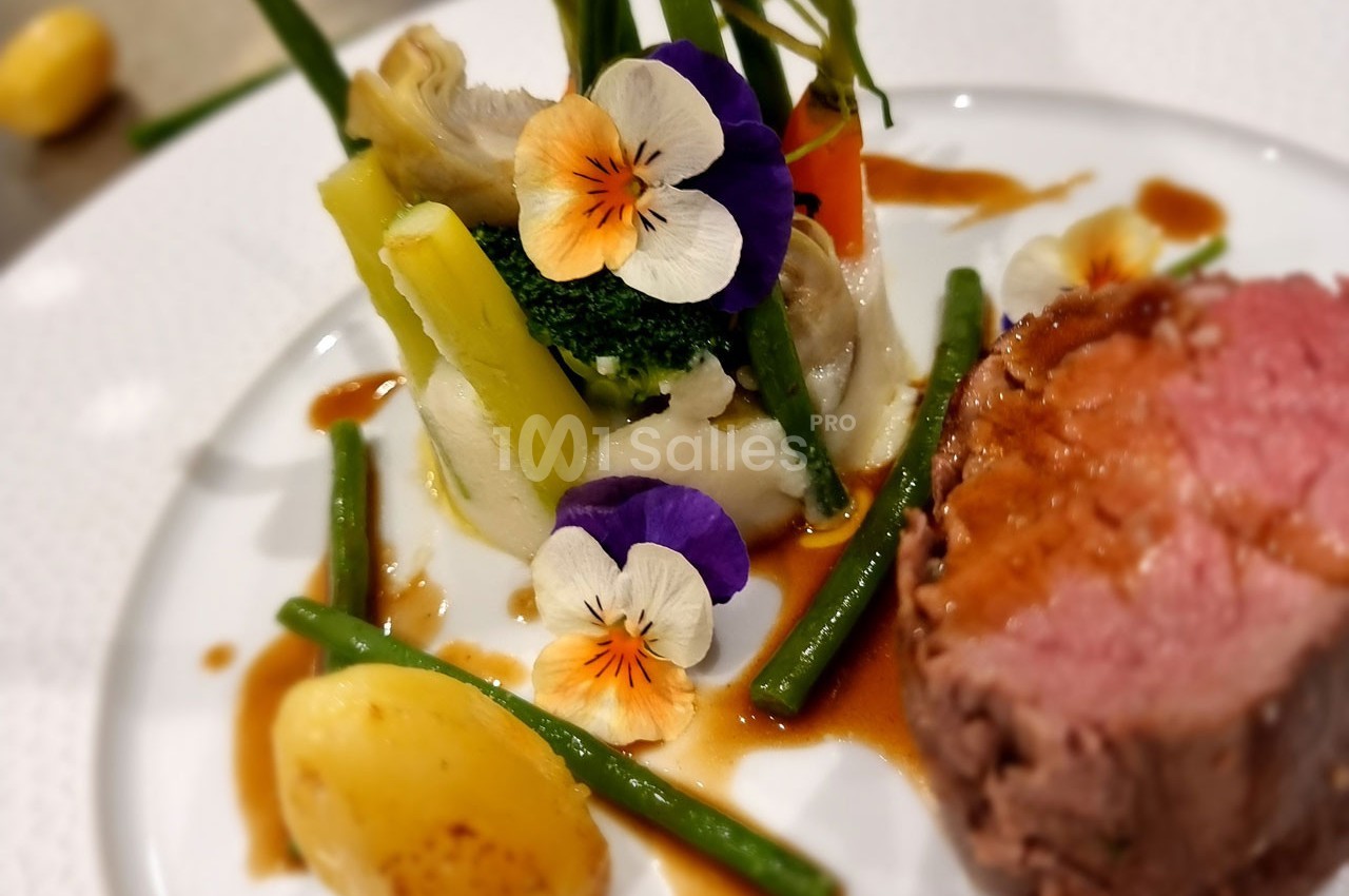 Assiette gastronomique avec viande rosée, légumes verts, purée, pommes de terre et fleurs comestibles en décoration.