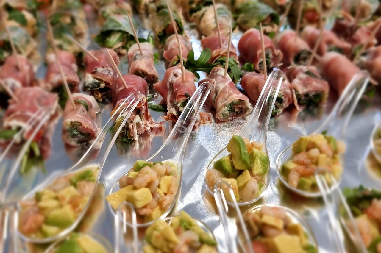 Bouchées apéritives composées de roulés de jambon cru et de cuillères garnies de crevettes, avocat et légumes.