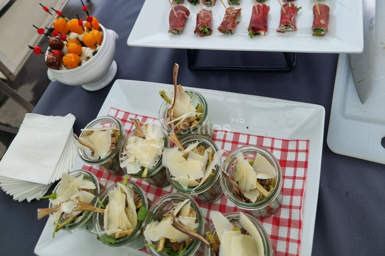 Assortiment d'entrées comprenant verrines de salade, brochettes de tomates cerises et roulés de jambon cru.