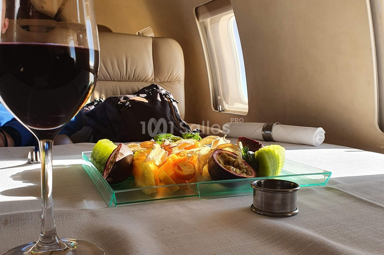Assiette de fruits frais et verre de vin rouge sur une table dressée dans un intérieur d'avion privé.