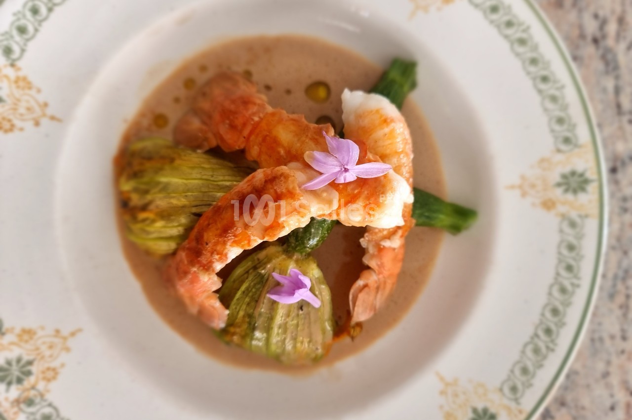 Assiette gastronomique avec fleurs de courgettes farcies, langoustines et sauce, décorée de fleurs comestibles.