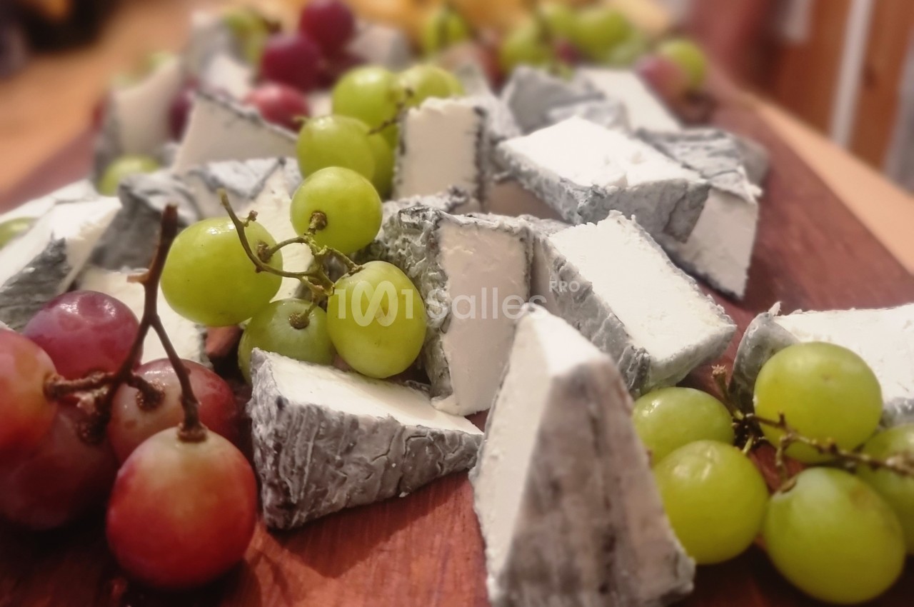 Assortiment de morceaux de fromage à croûte cendrée entourés de raisins verts et rouges sur une planche en bois.