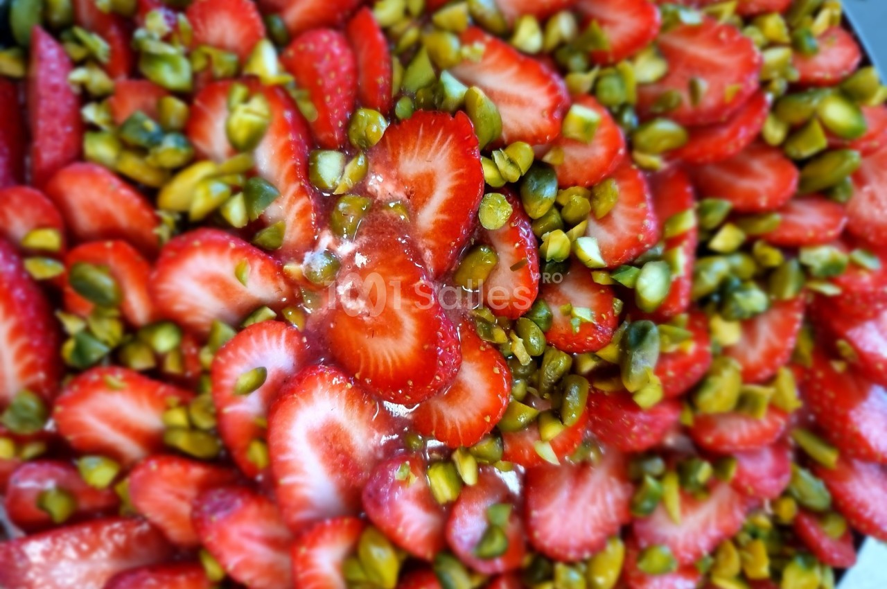 Tranches de fraises fraîches mélangées à des pistaches hachées, disposées en garniture colorée.
