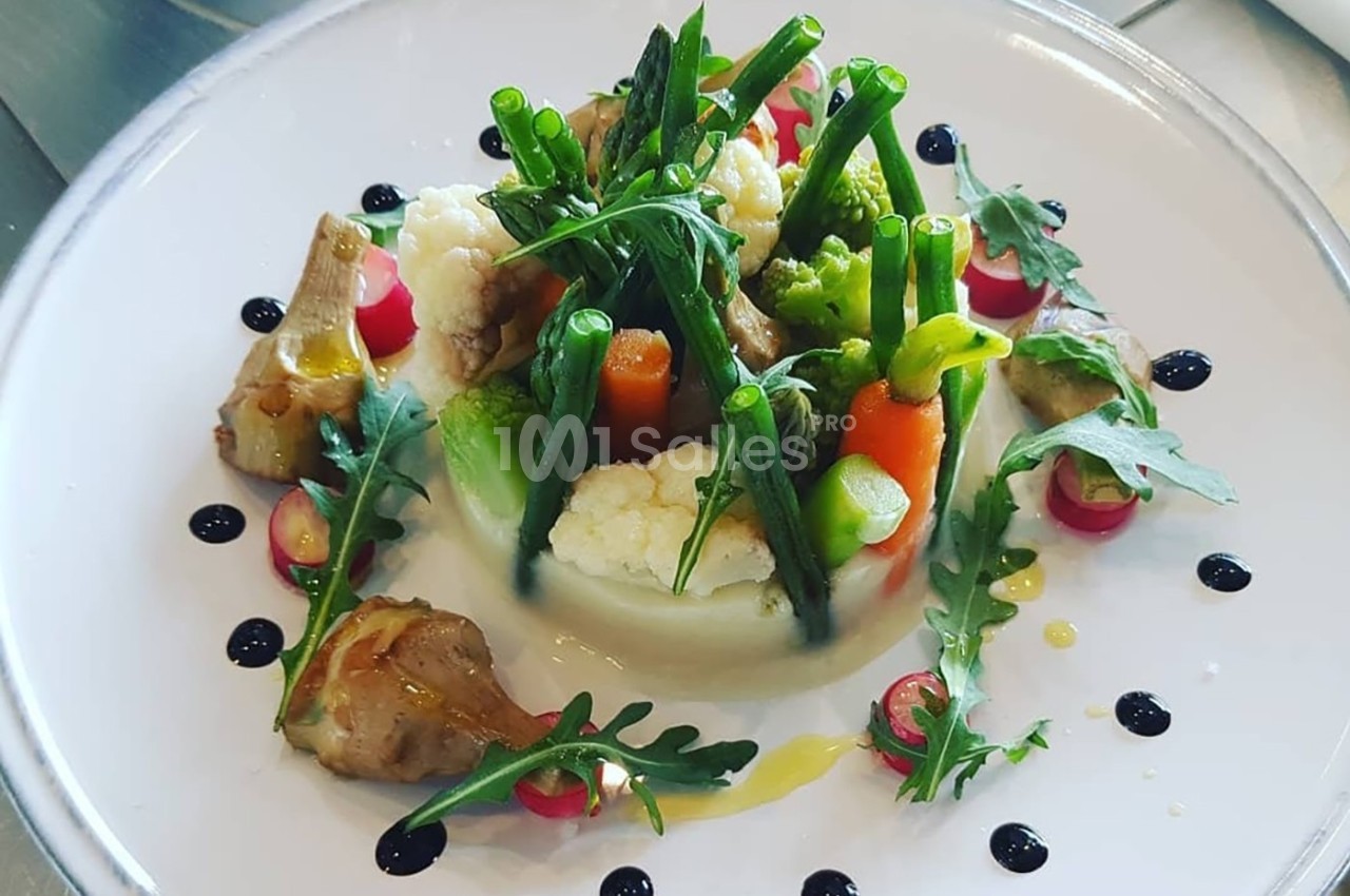 Assiette de légumes variés dressés avec soin, comprenant asperges, carottes, chou-fleur, roquette et sauce décorative.
