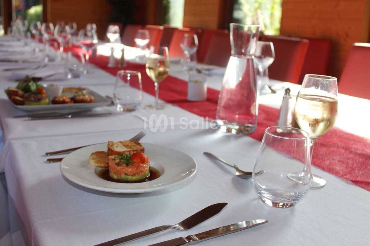 Table dressée avec une nappe blanche, des couverts, des verres à vin et une entrée servie sur une assiette blanche.