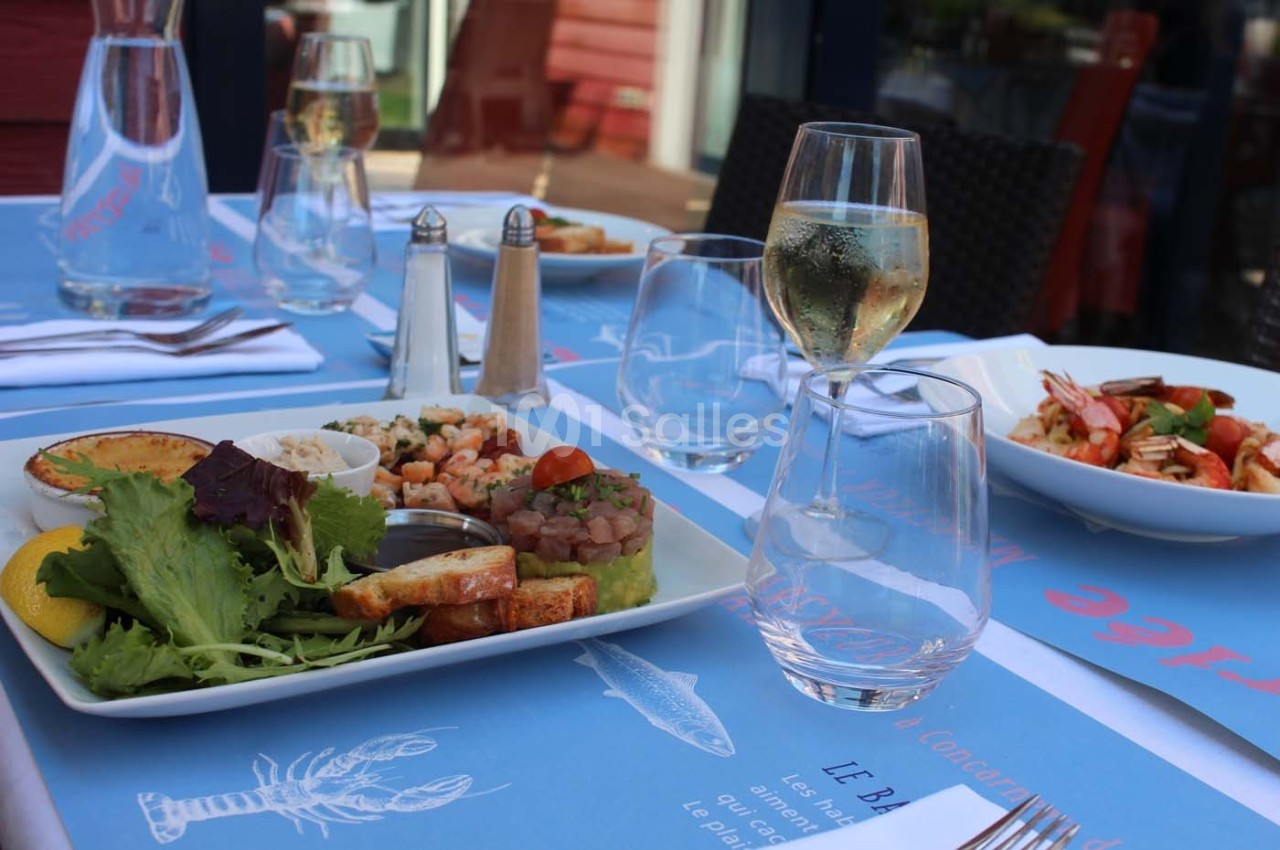 Table dressée en extérieur avec assiettes de fruits de mer, salade, pain grillé et verre de vin blanc.