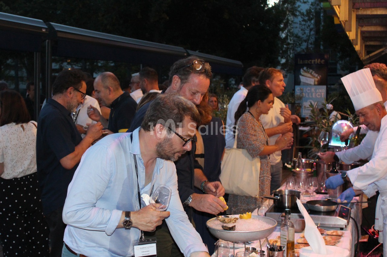 Des personnes se servent à un buffet en plein air, avec un chef en tenue blanche préparant des plats.