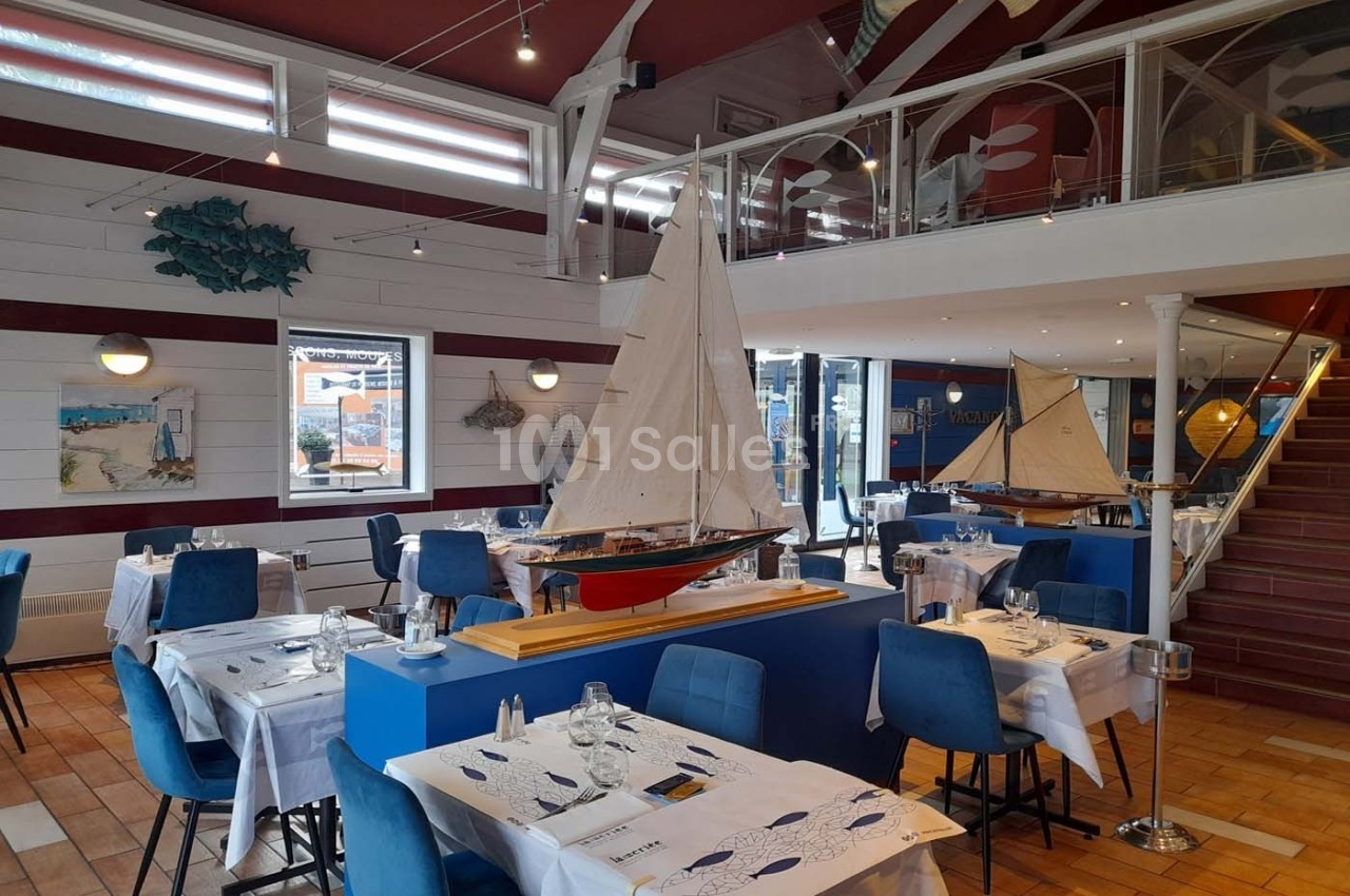 Salle de restaurant lumineuse décorée sur le thème de la mer avec des maquettes de voiliers et des tables dressées.