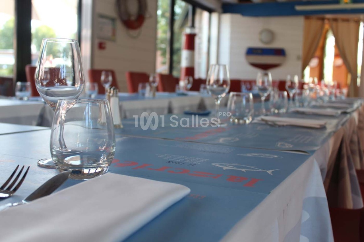 Tables dressées avec nappes bleues, verres et serviettes blanches dans un restaurant lumineux avec vue sur l'extérieur.