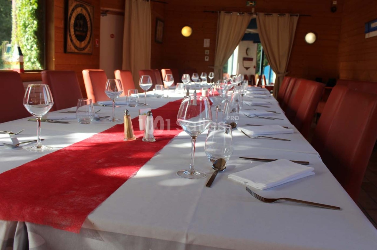 Table dressée avec une nappe blanche et un chemin de table rouge, entourée de chaises rouges dans une salle lumineuse.