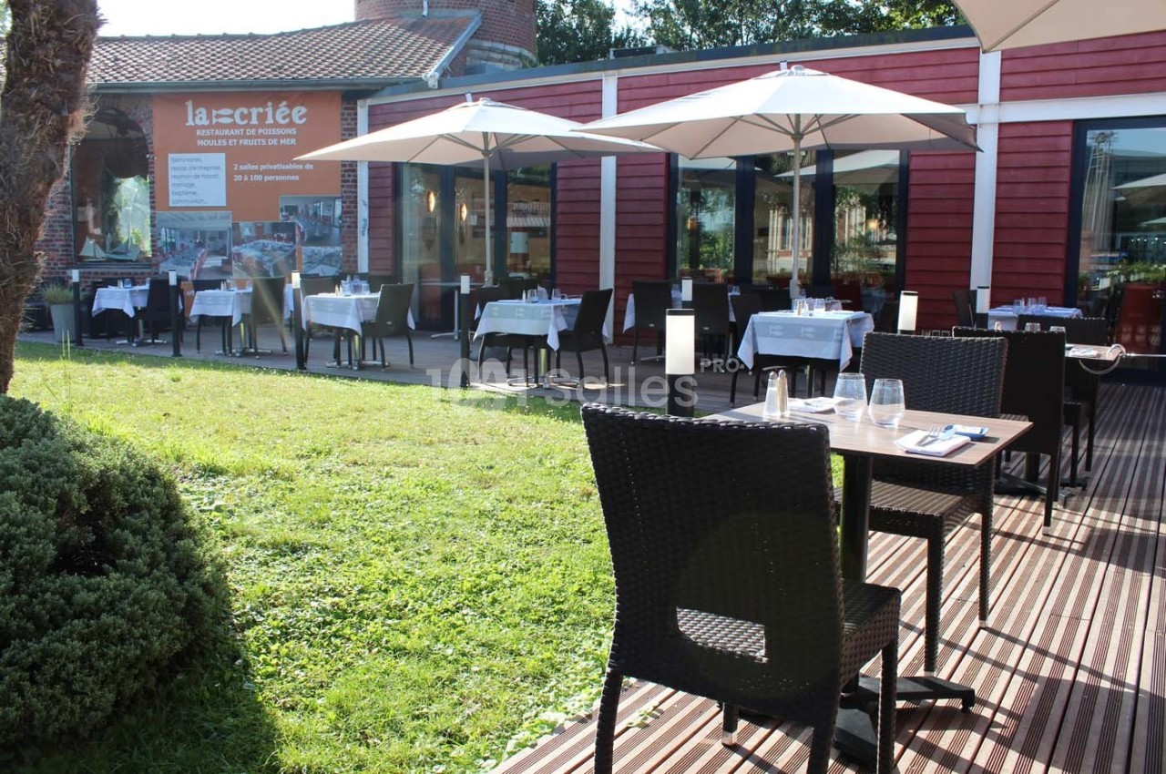 Terrasse d'un restaurant avec tables dressées, parasols blancs et façade rouge en arrière-plan.
