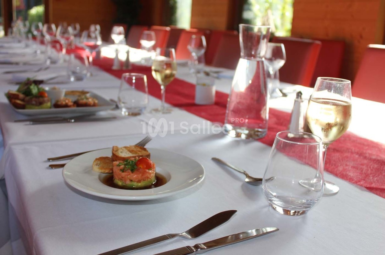 Table dressée avec une nappe blanche, des couverts, des verres à vin et une entrée servie sur une assiette blanche.