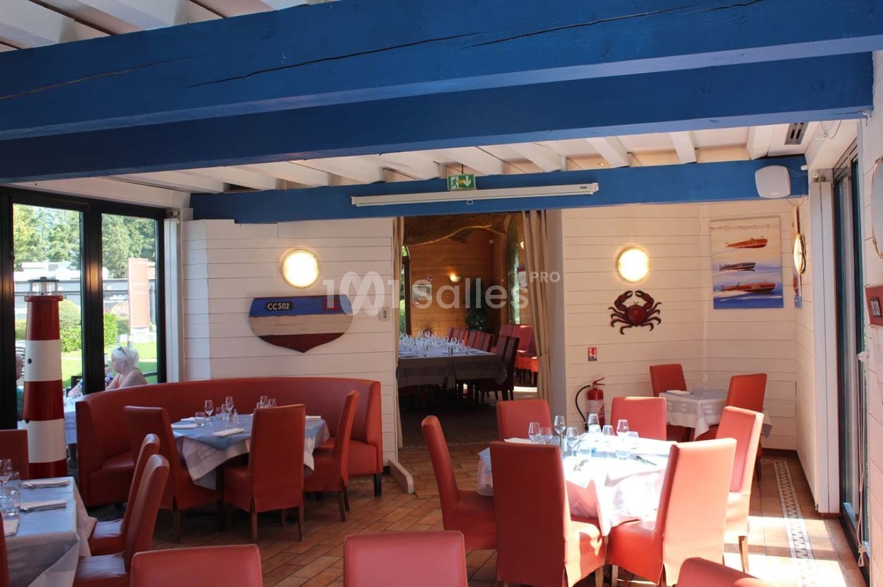 Salle de restaurant lumineuse avec tables dressées, chaises rouges et décoration maritime sur les murs.