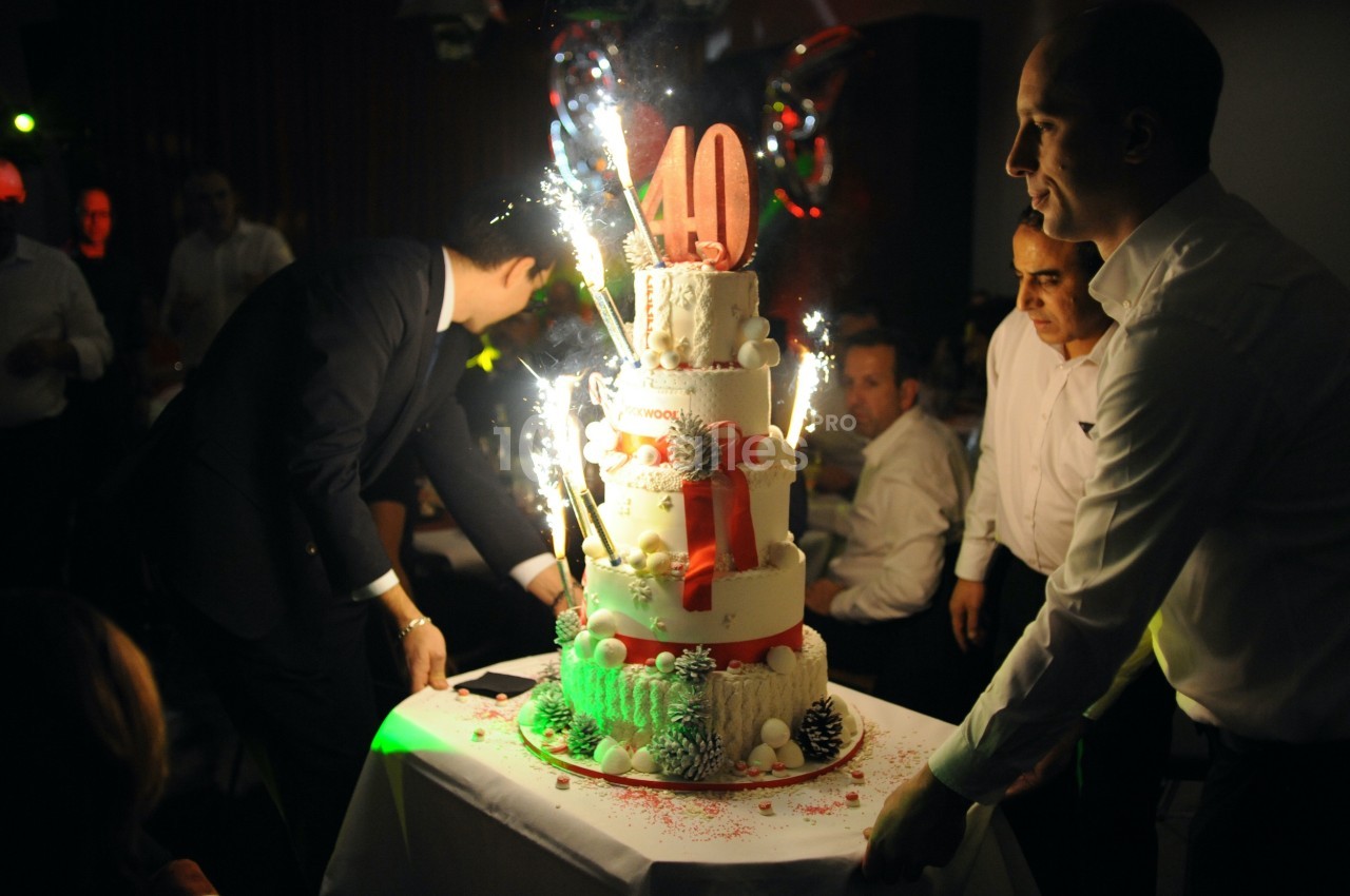 Deux hommes portent un grand gâteau décoré de bougies étincelantes et du chiffre 40 lors d'une fête.