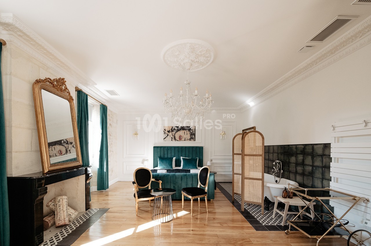 Chambre élégante avec lit double, baignoire sur pieds, miroir doré, mobilier vert et détails décoratifs raffinés.
