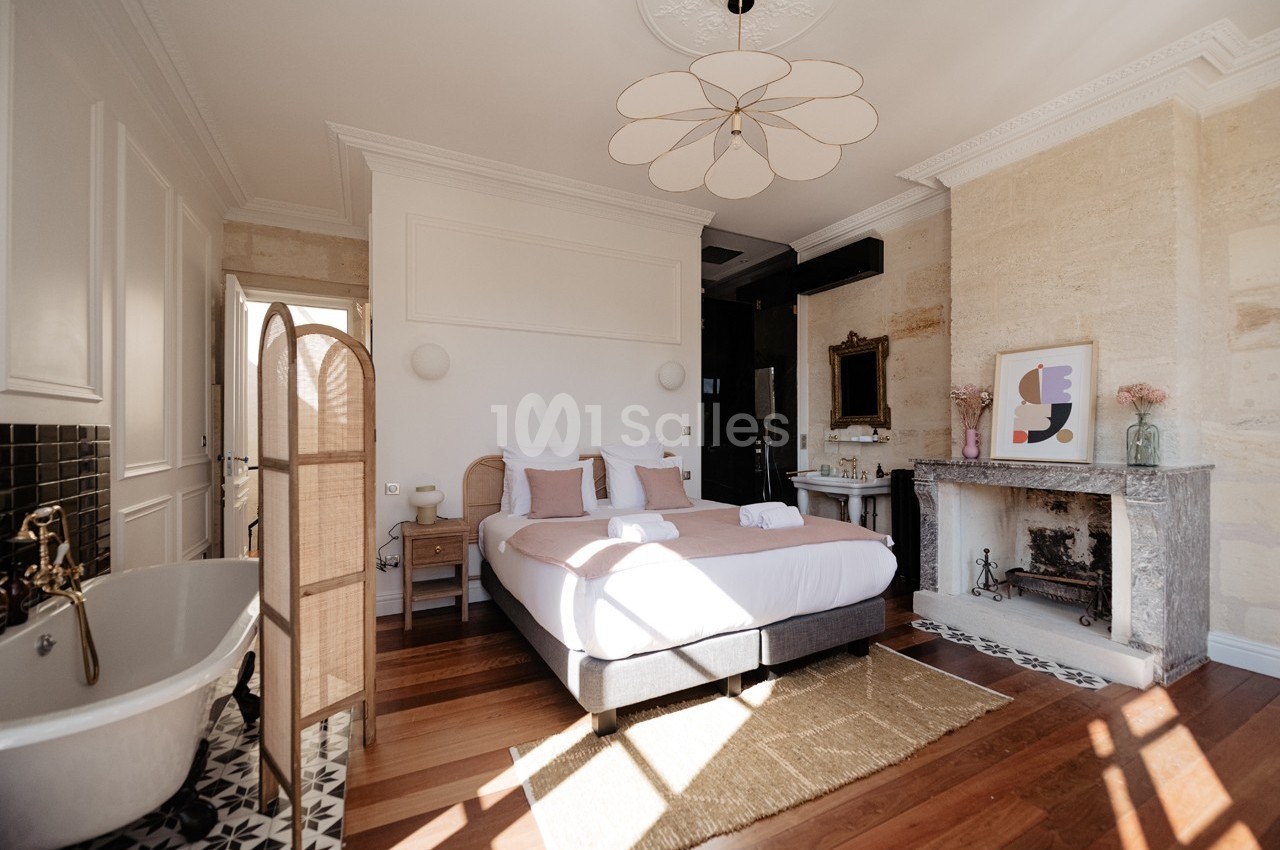 Chambre lumineuse avec lit double, baignoire sur pieds, cheminée en pierre et décoration élégante.