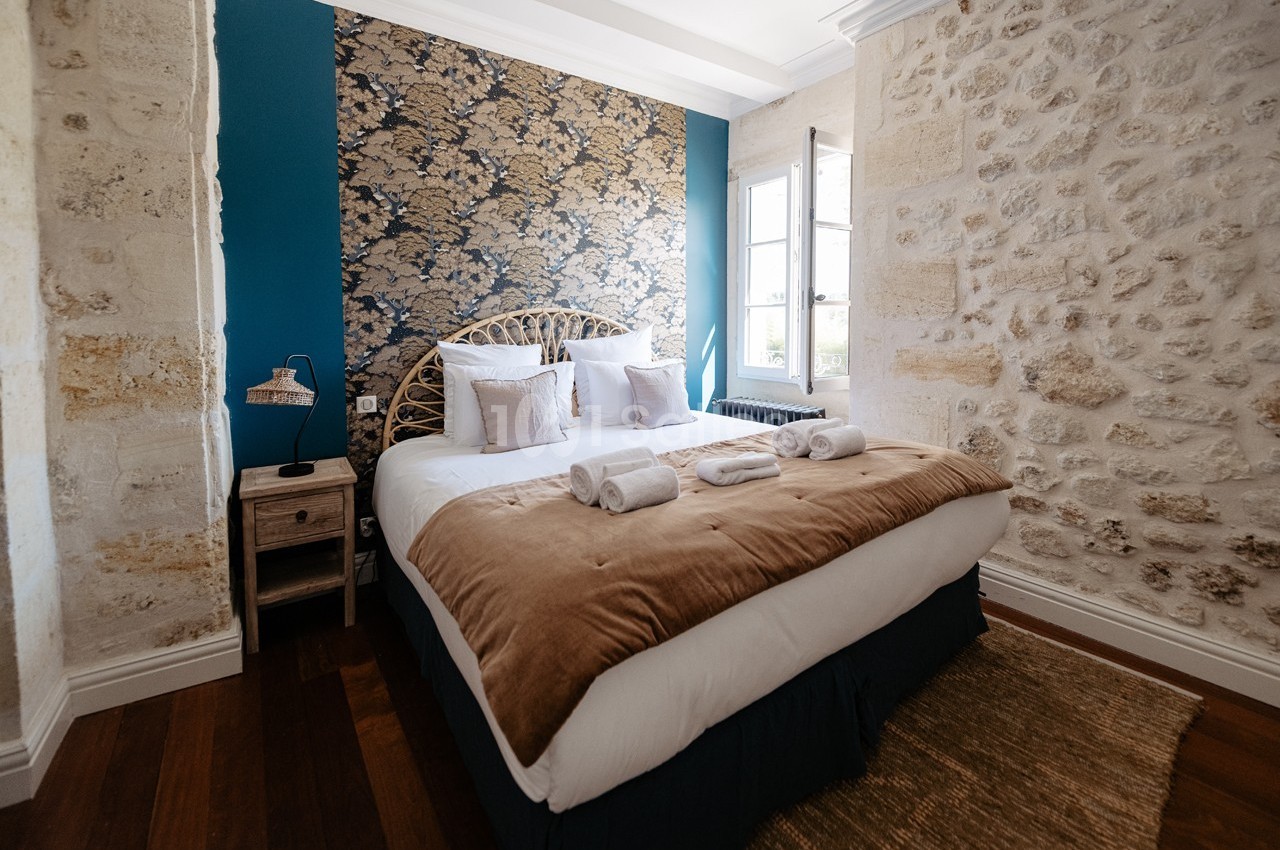 Chambre lumineuse avec lit double, murs en pierre apparente, tête de lit en rotin et fenêtre donnant sur l'extérieur.
