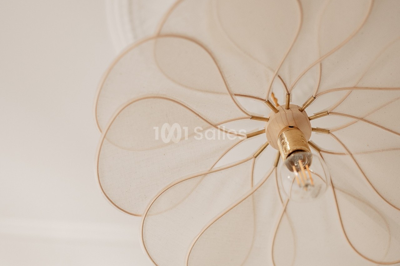 Suspension lumineuse en tissu beige clair avec une ampoule visible, vue en contre-plongée.