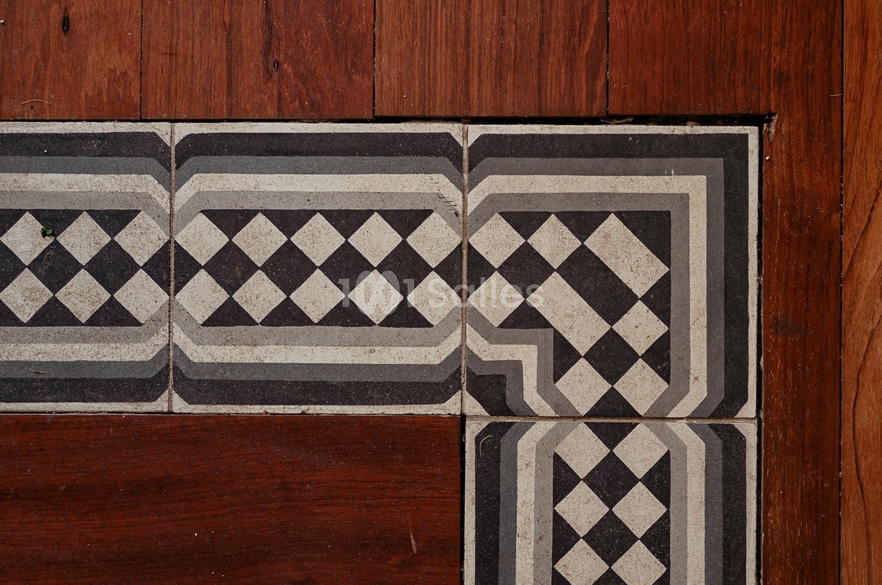 Carreaux en noir et blanc à motifs géométriques bordant un parquet en bois brun.