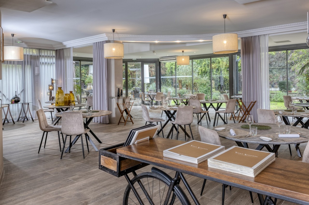 Salle de restaurant lumineuse avec grandes baies vitrées, tables espacées et décoration moderne.