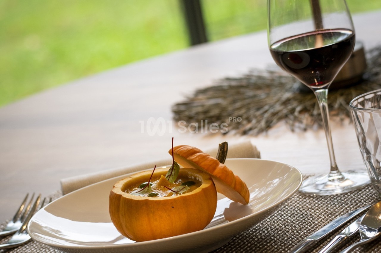 Une soupe servie dans une petite citrouille, accompagnée d'un verre de vin rouge sur une table dressée.