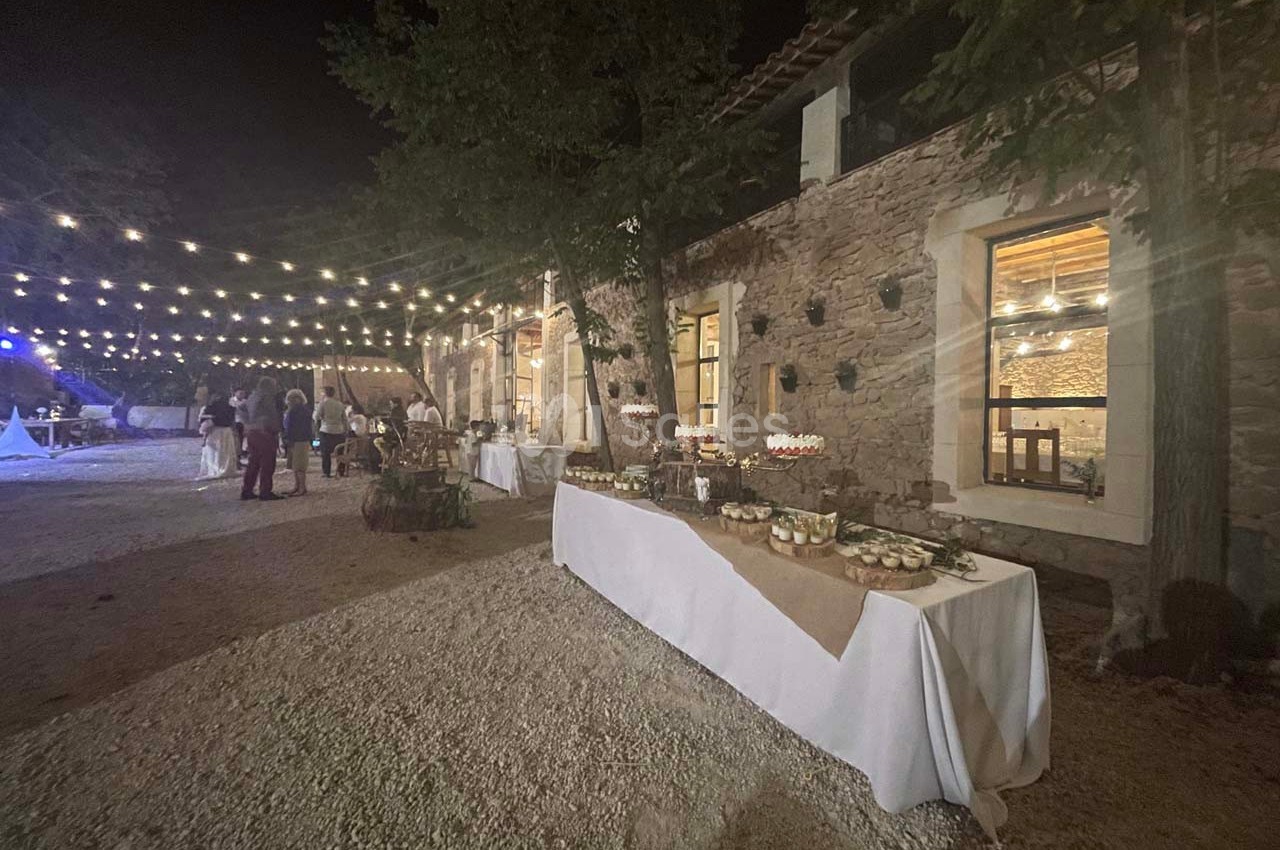 Tables décorées avec des desserts et des lumières suspendues dans une cour extérieure en soirée.