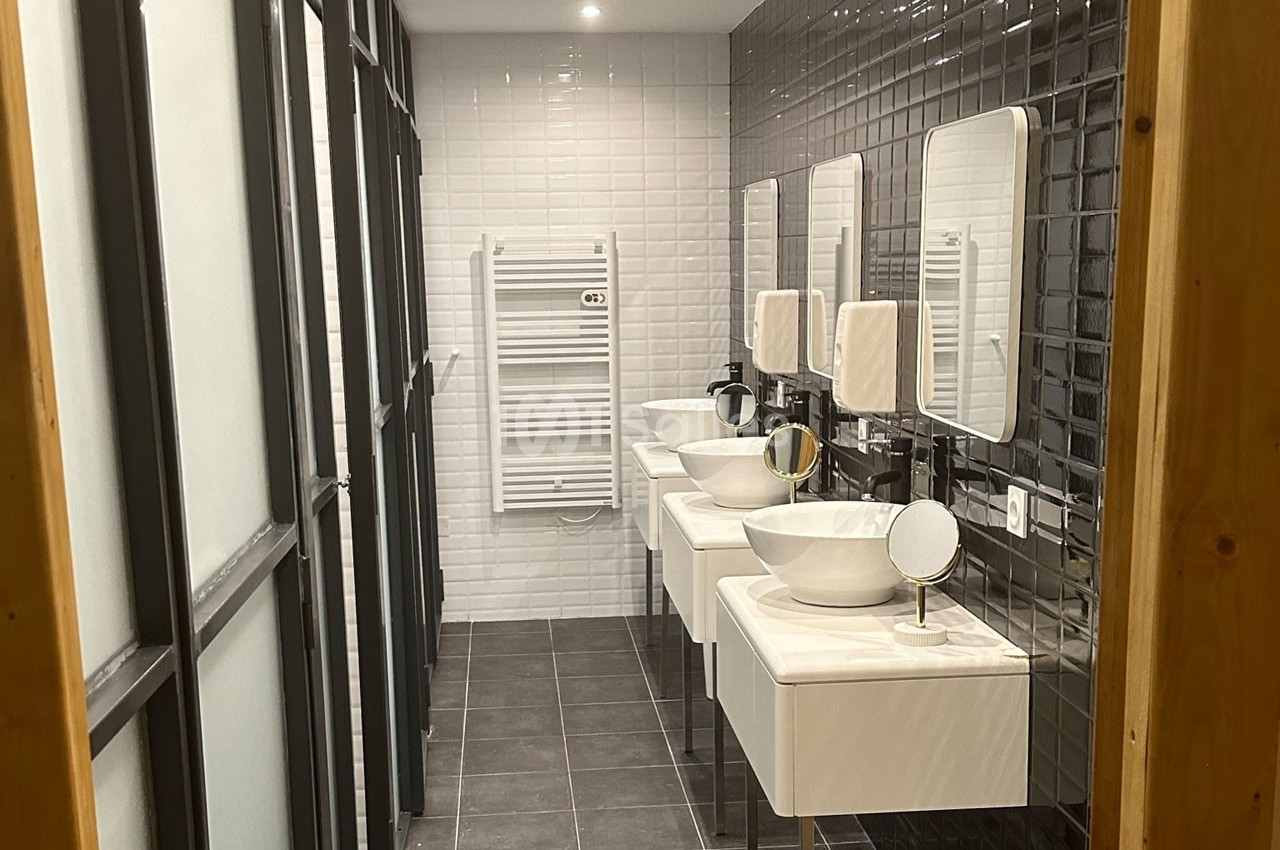 Salle de bain moderne avec trois lavabos, miroirs, carrelage noir et blanc, et un sèche-serviettes mural.